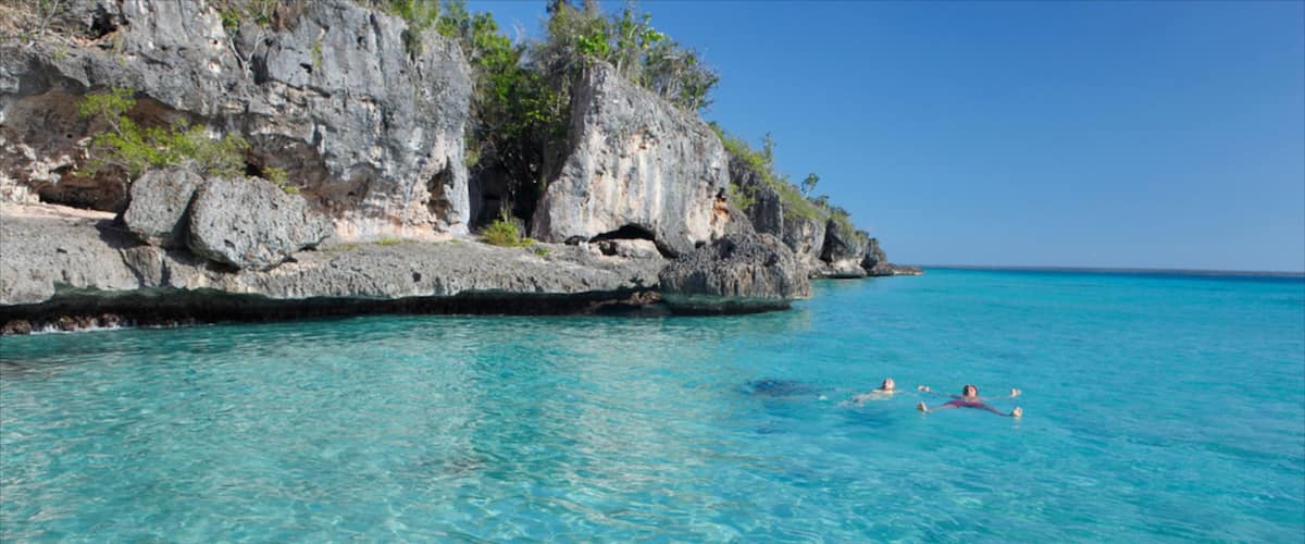 A clear turquoise sea with rocky cliffs and a few people swimming.