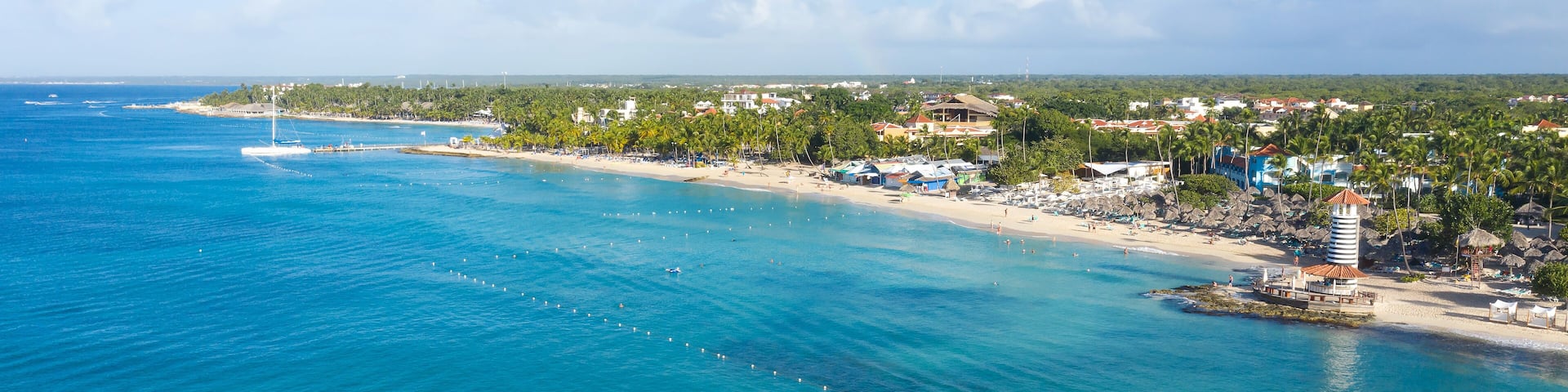 A coastal town with a beach, palm trees, and a lighthouse.