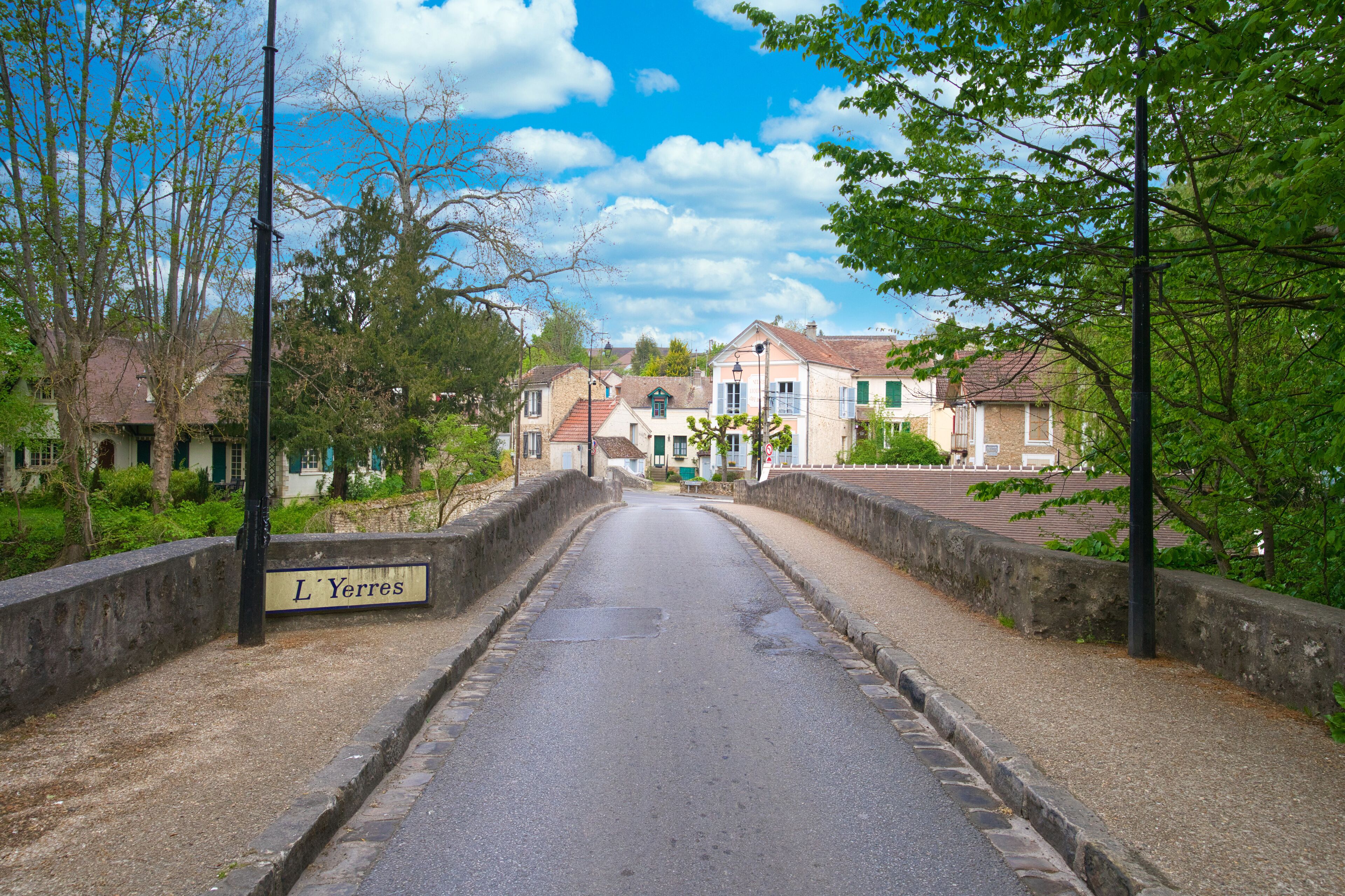 A narrow street named L'Yerres with stone walls on either side, leading to a row of traditional houses with red roofs.