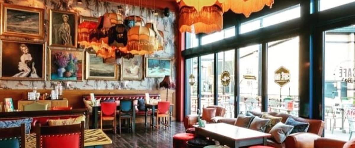 A cozy restaurant with wooden floors, red and blue chairs, and a large hanging light fixture.