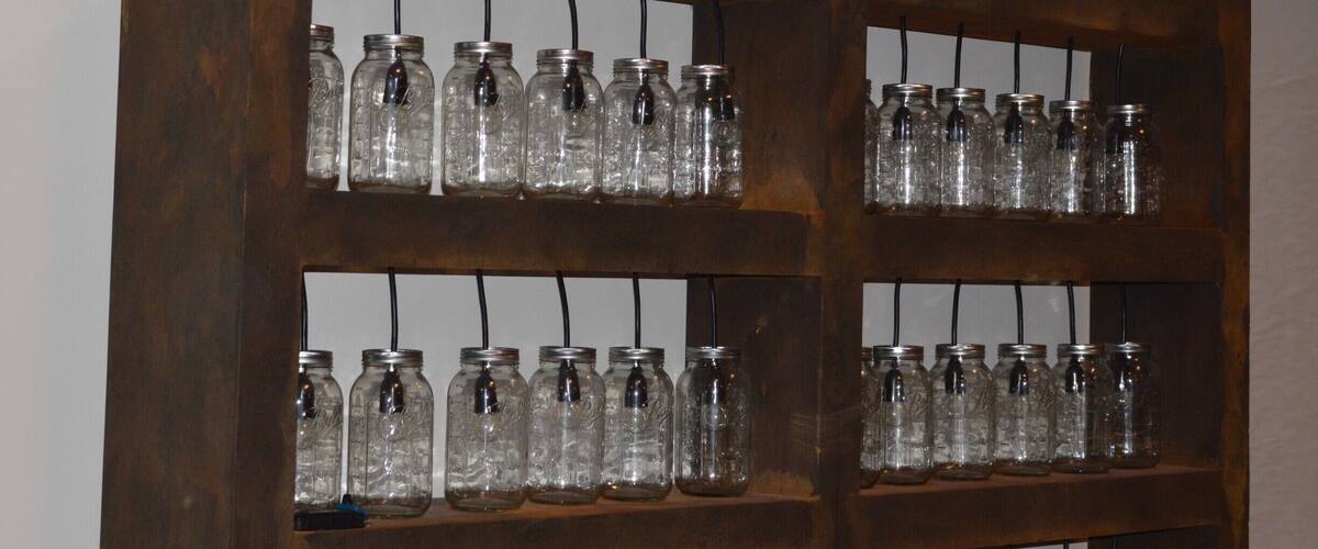A wooden display shelf with multiple rows of empty glass jars.