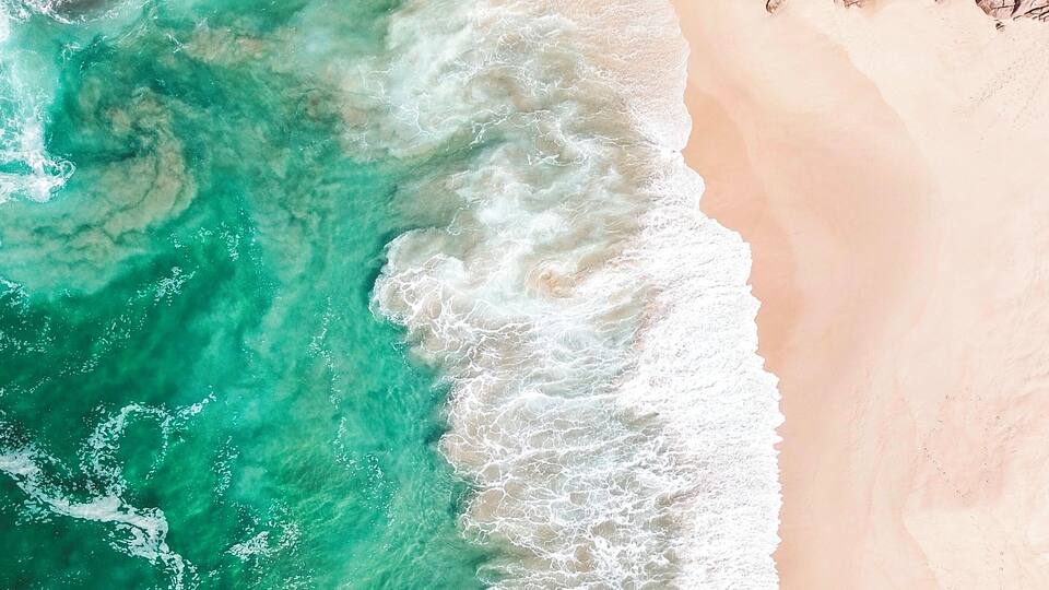 An aerial view of a beach with turquoise waters and rocky cliffs.