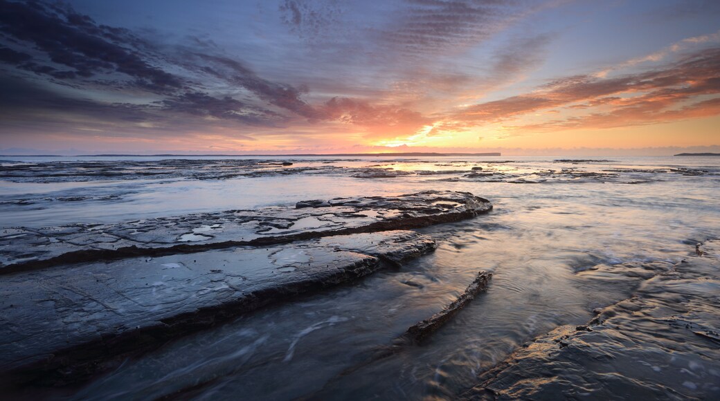 Un rivage rocheux au coucher du soleil, avec un ciel aux couleurs éclatantes.