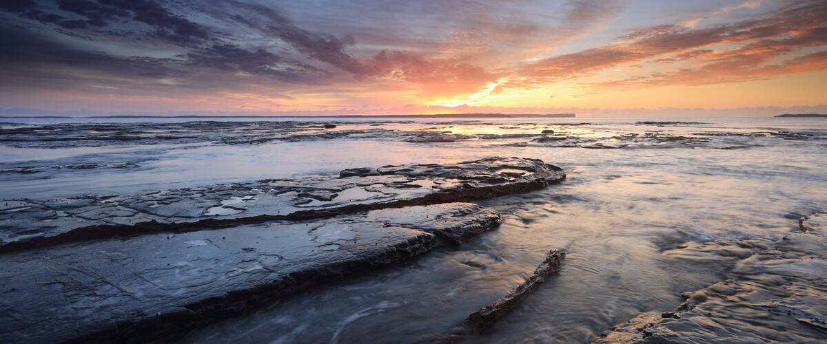 A rocky shoreline at sunset with a vibrant sky.