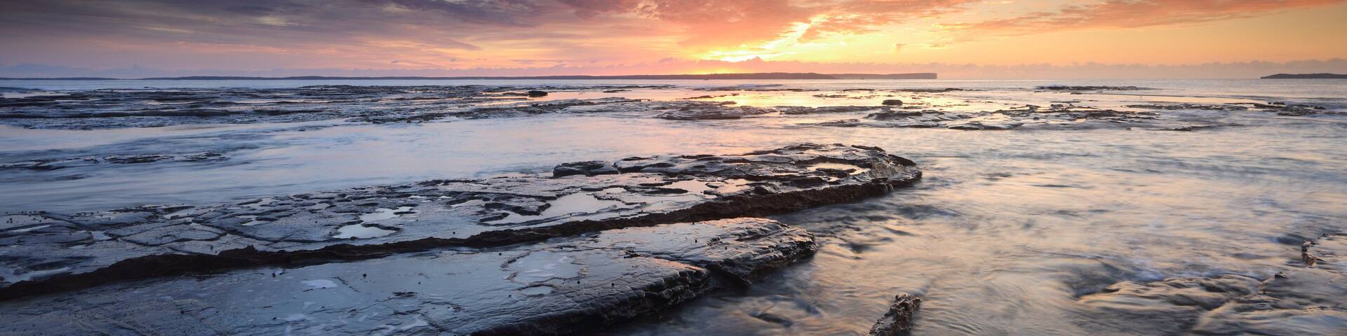 A rocky shoreline at sunset with a vibrant sky.