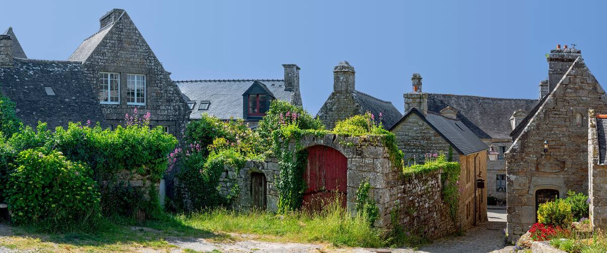 A stone building with a red door and a stone wall with greenery.