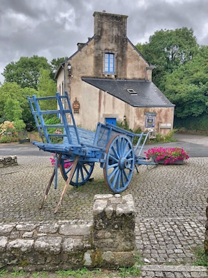 A blue cart in front of a rustic building with a blue door and a sign that reads "From Us."