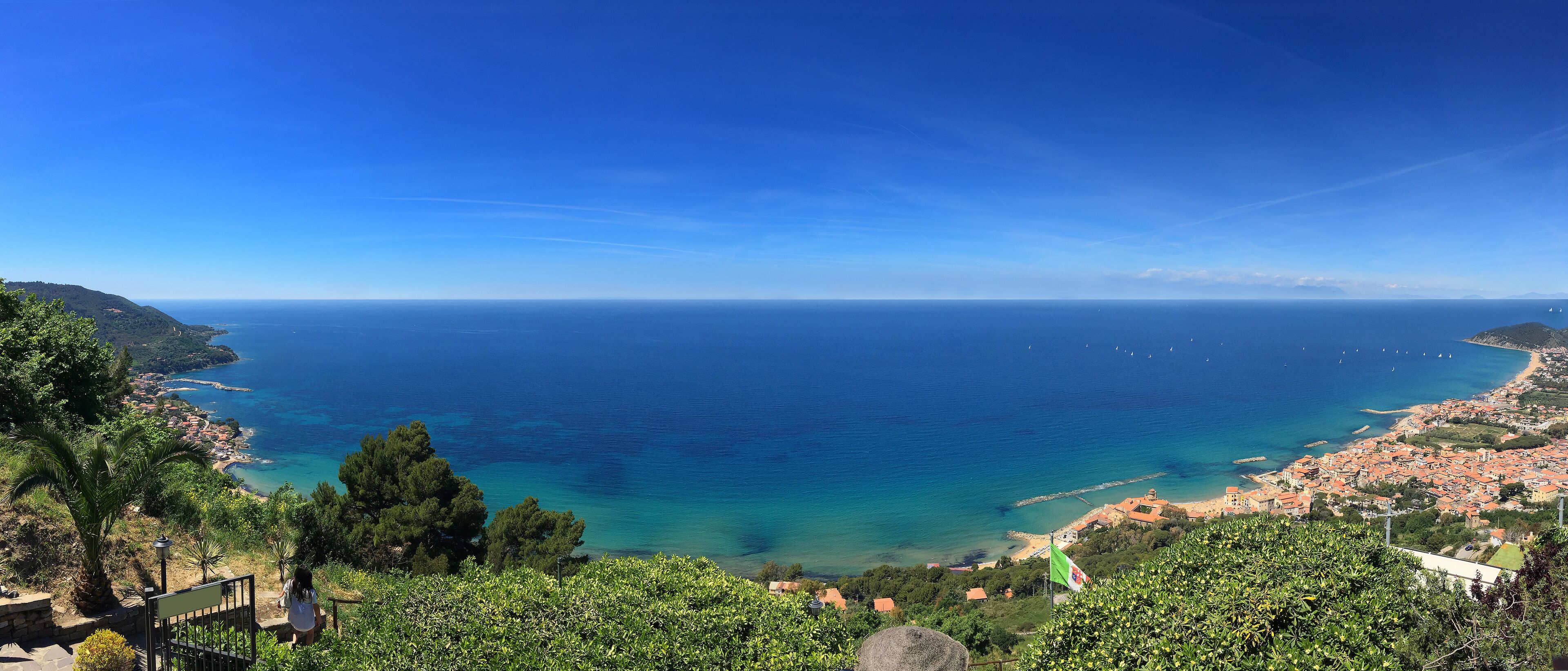 A coastal town with a clear view of the sea, lush greenery, and a distant shoreline.