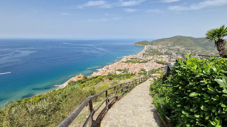A coastal town with a wooden walkway overlooking the sea and mountains.
