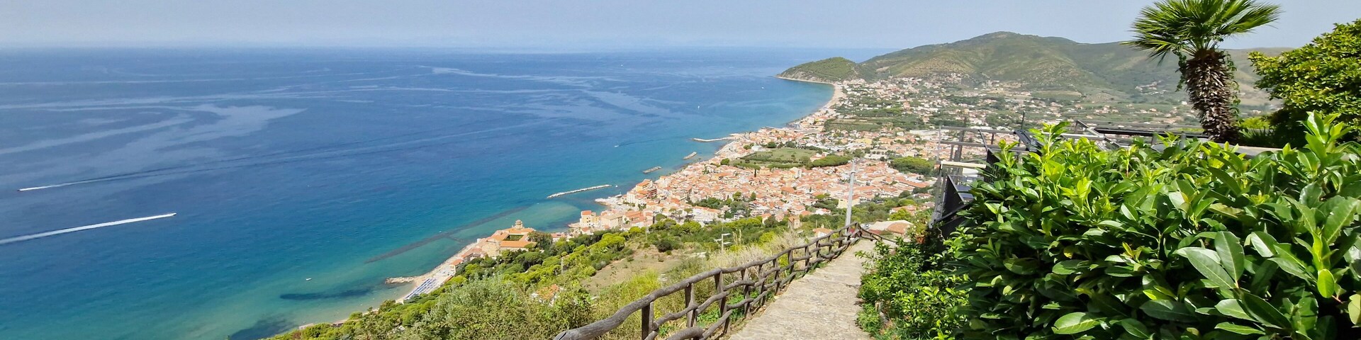 Un pueblo costero con un paseo de madera que da vista al mar y a las montañas.