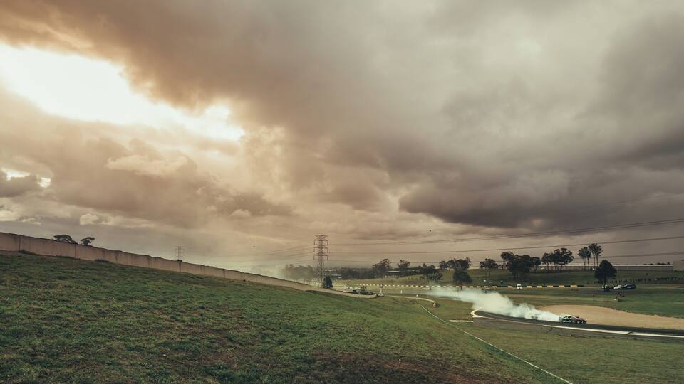 A grassy hill with a road curving through it, a power line tower, and a cloudy sky.