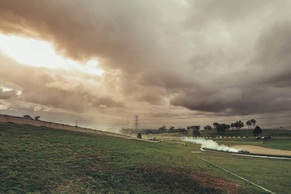 A grassy hill with a road curving through it, a power line tower, and a cloudy sky.