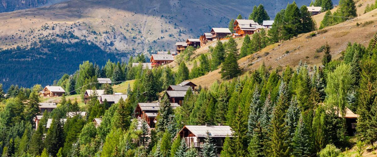 A mountain village with wooden houses nestled among trees, with a prominent mountain peak in the background.