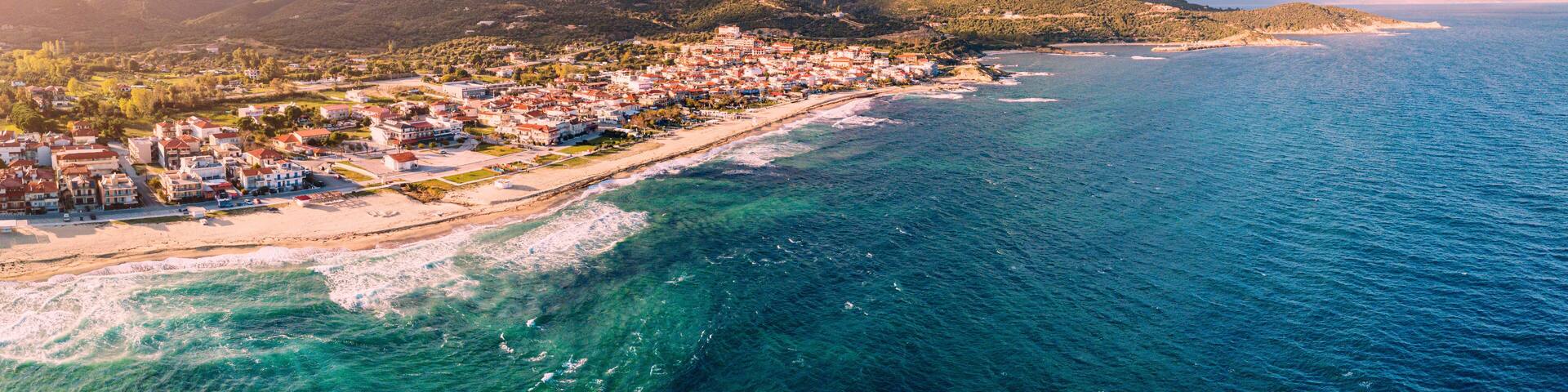 Dramatic panoramic aerial view of iconic Sarti resort town and famous long and empty sandy beach at sunset time with high waves. Vacation on Halkidiki, Greece