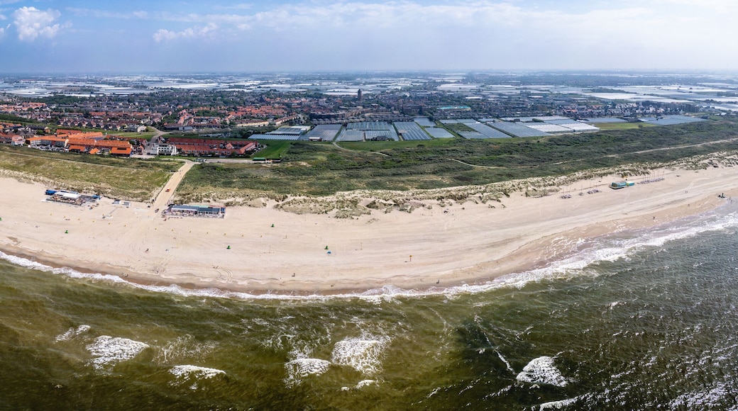 A panoramic view of Ter Heijde village shows an expansive sandy beach curving around a body of water, with buildings and farmland visible in the background.