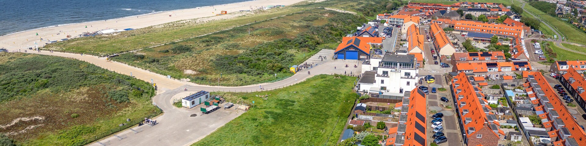 Un pueblo costero con playa, campos verdes y edificios de tejados naranjas.