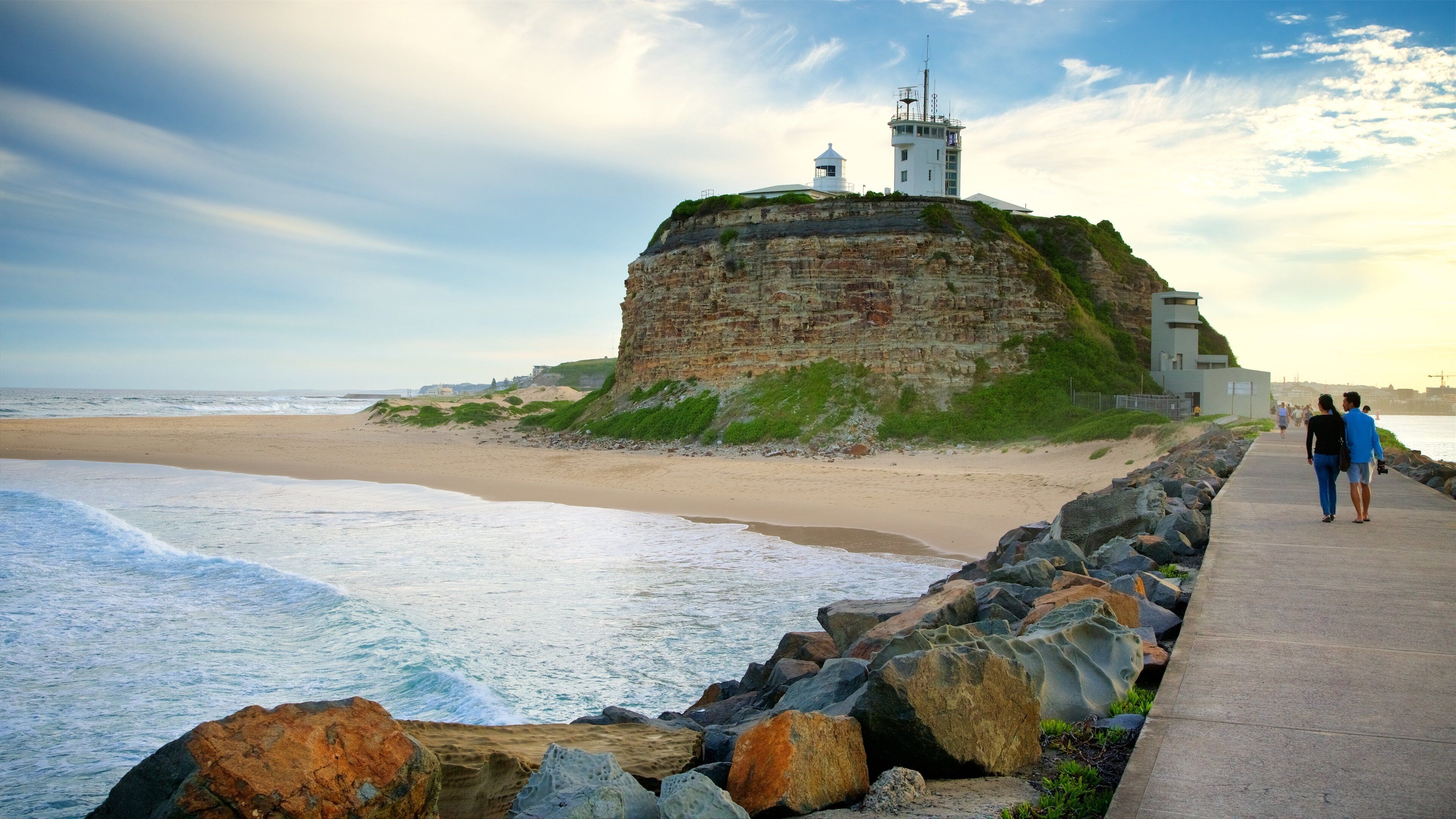 Paisagem costeira com um penhasco imponente, um farol e uma praia.