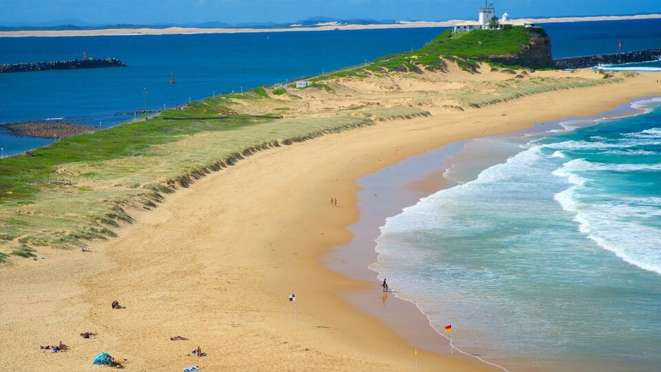 A sandy beach with waves, a lighthouse, and a rocky outcrop.