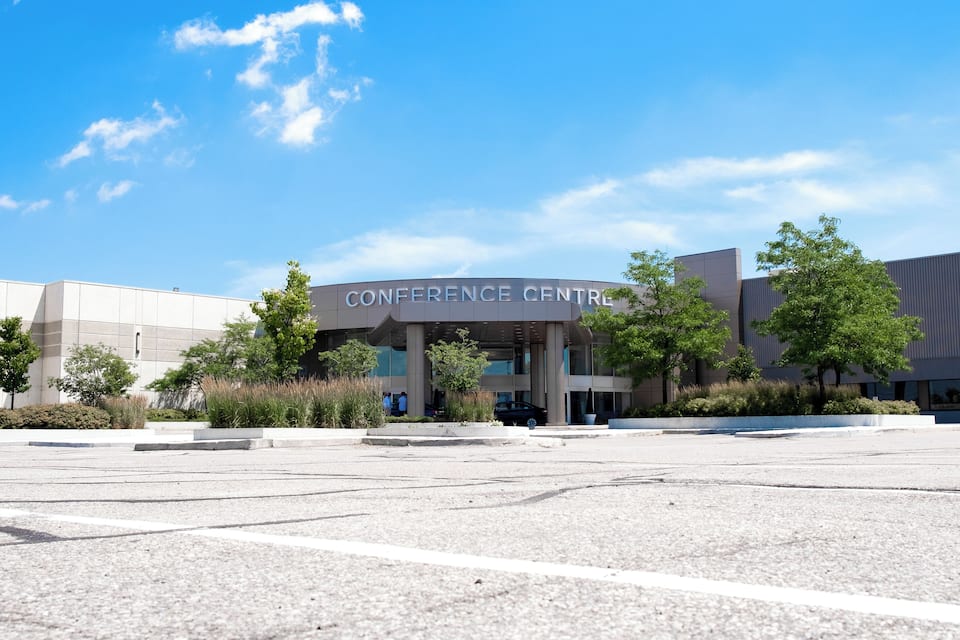 A modern conference center with a clear blue sky and trees in the foreground.
