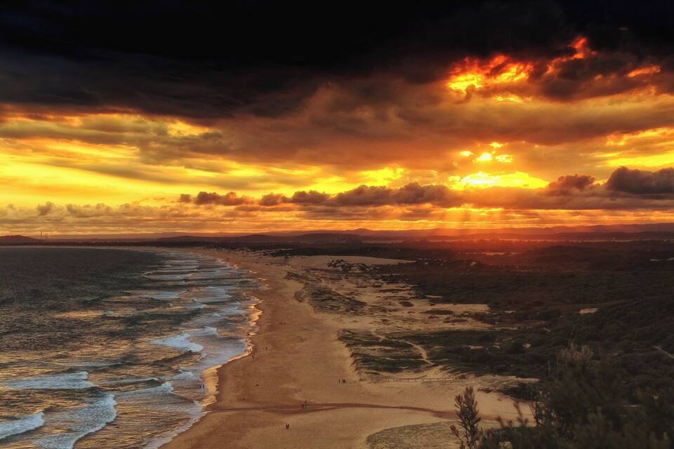 A beach with waves, a sandy shore, and a sunset.