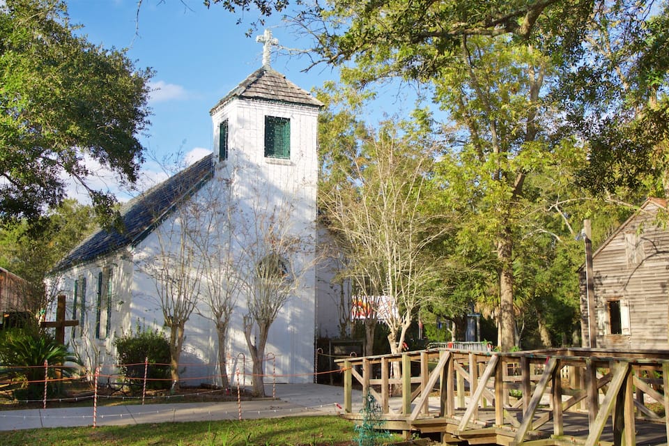 A white church with a steeple, surrounded by trees and a wooden bridge.