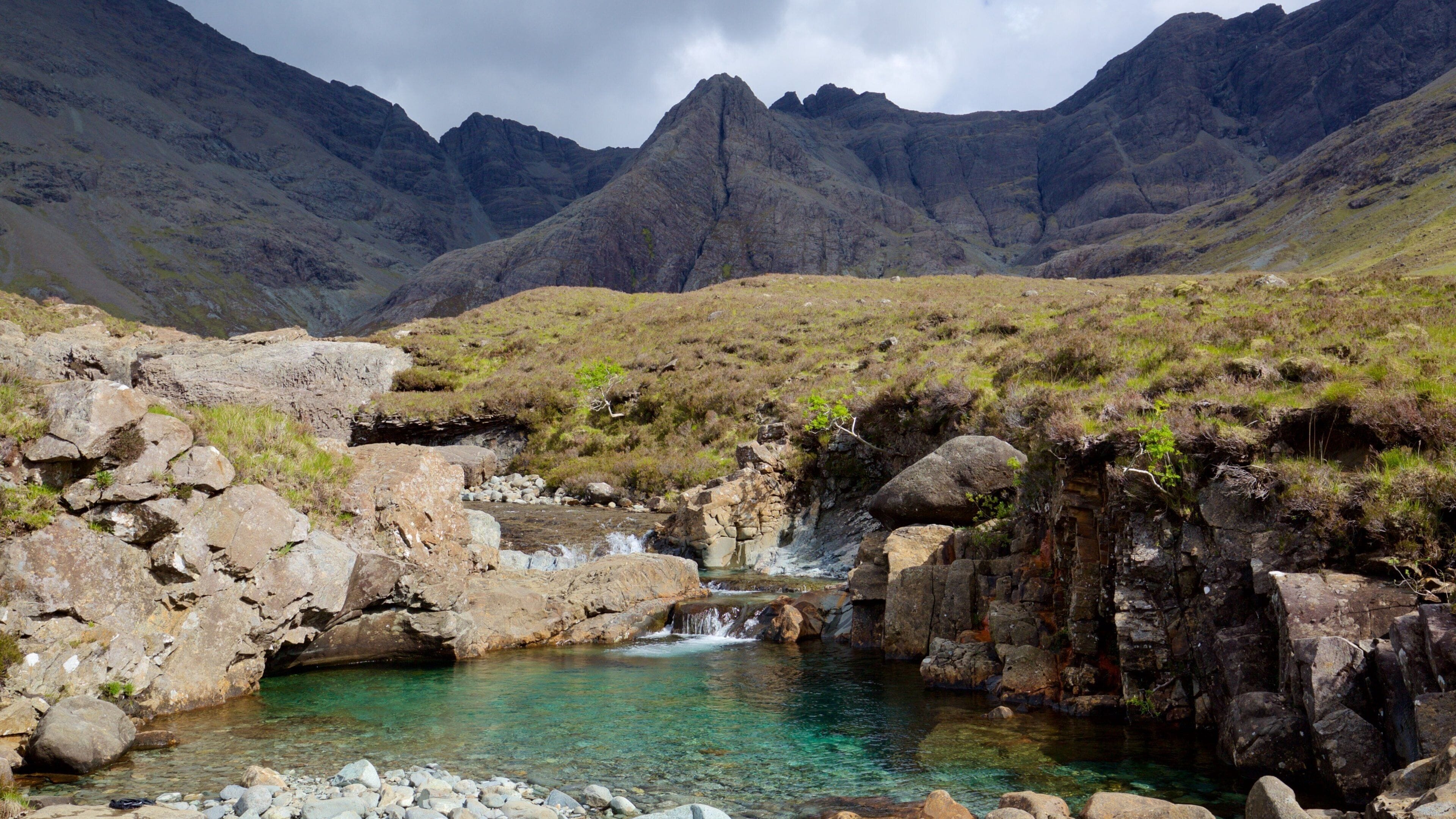 A clear mountain stream surrounded by rocky terrain and sparse vegetation.
