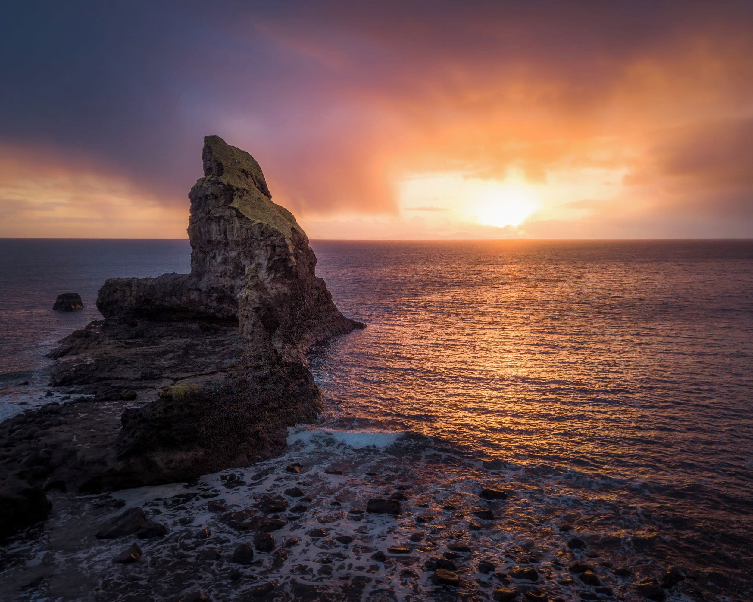 A rocky coastline with a prominent rock formation during sunset.