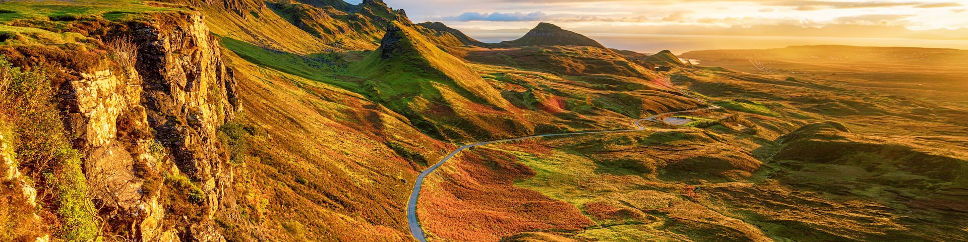Una carretera sinuosa que serpentea por un valle con riscos rocosos y terreno cubierto de pasto.
