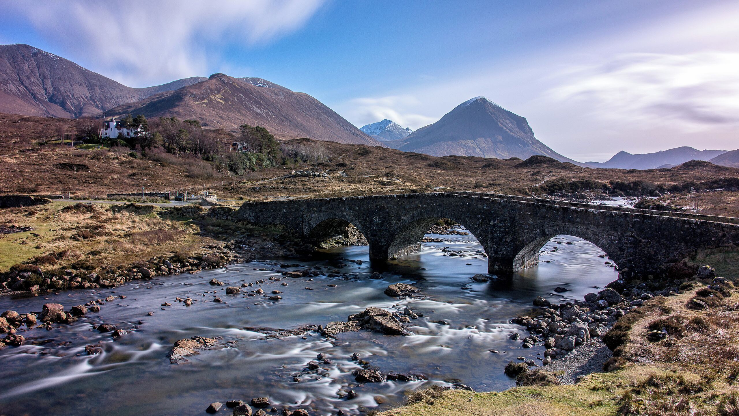 A stone bridge over a river with mountains in the background.