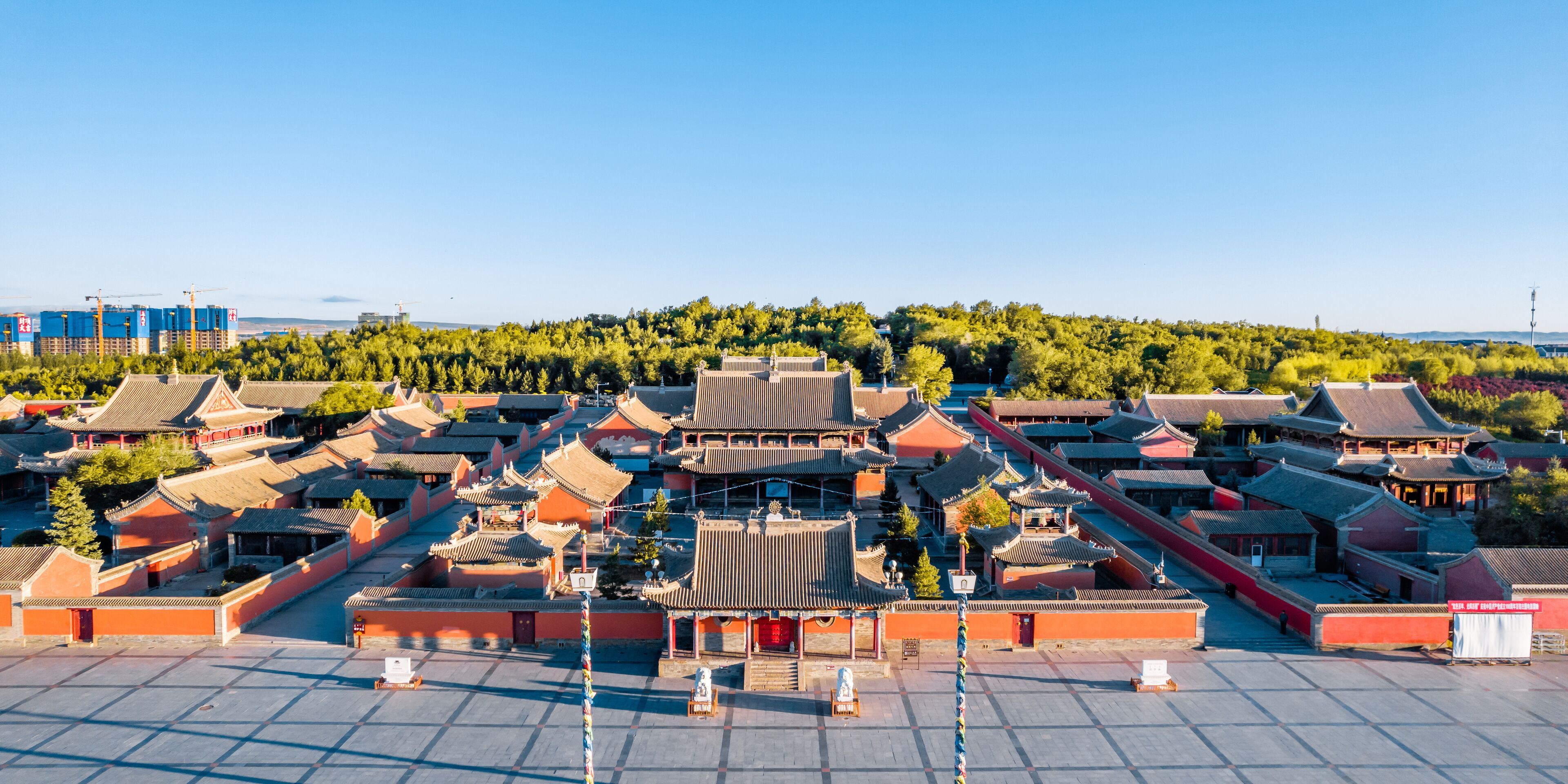A traditional Chinese architectural complex with red walls and tiled roofs, surrounded by greenery and a clear blue sky.