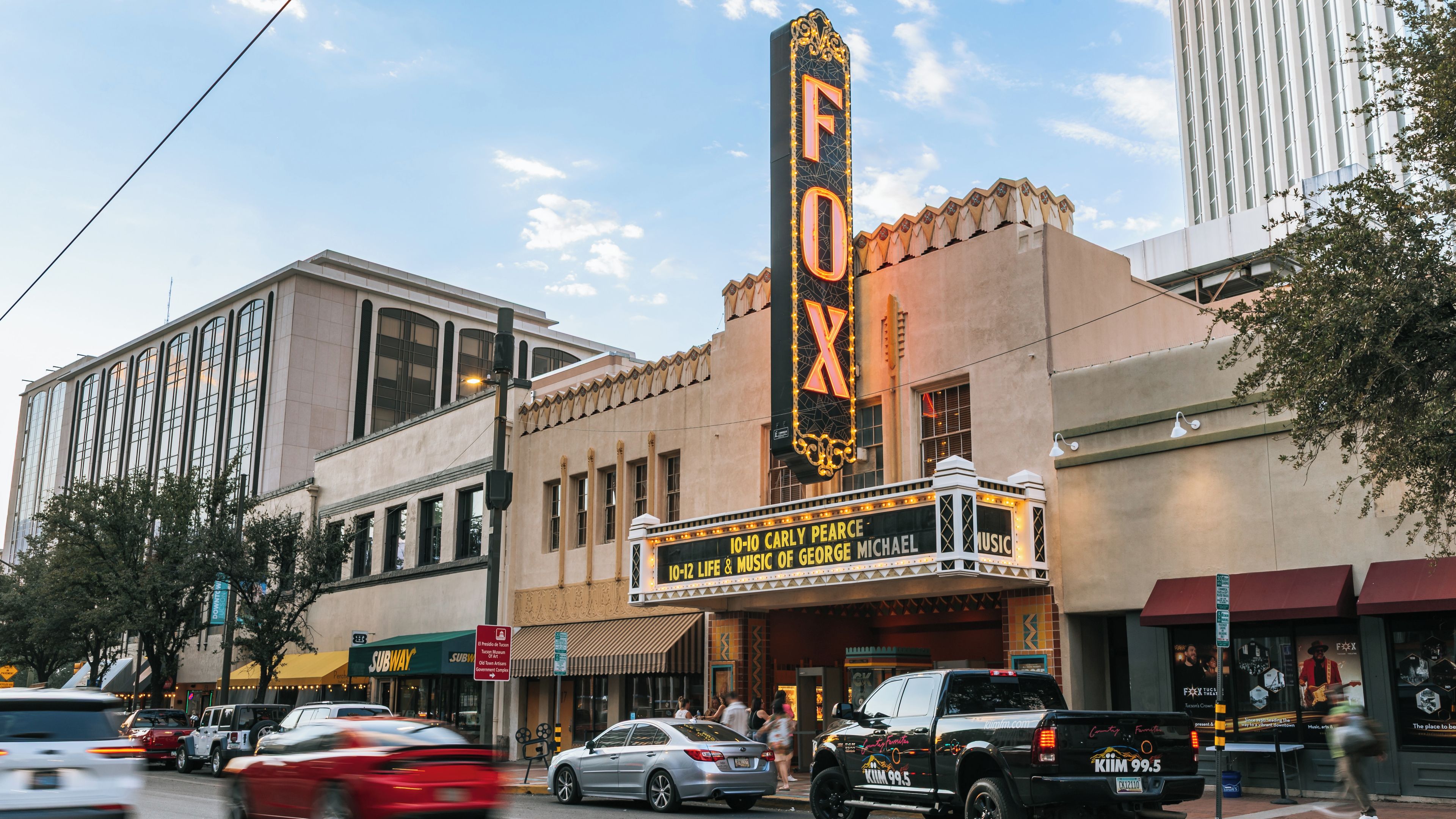 A theater with a marquee advertising a musical, surrounded by urban buildings and vehicles.