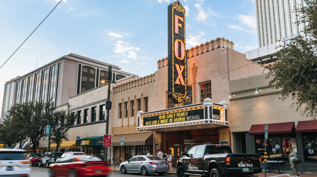 A theater with a marquee advertising a musical, surrounded by urban buildings and vehicles.