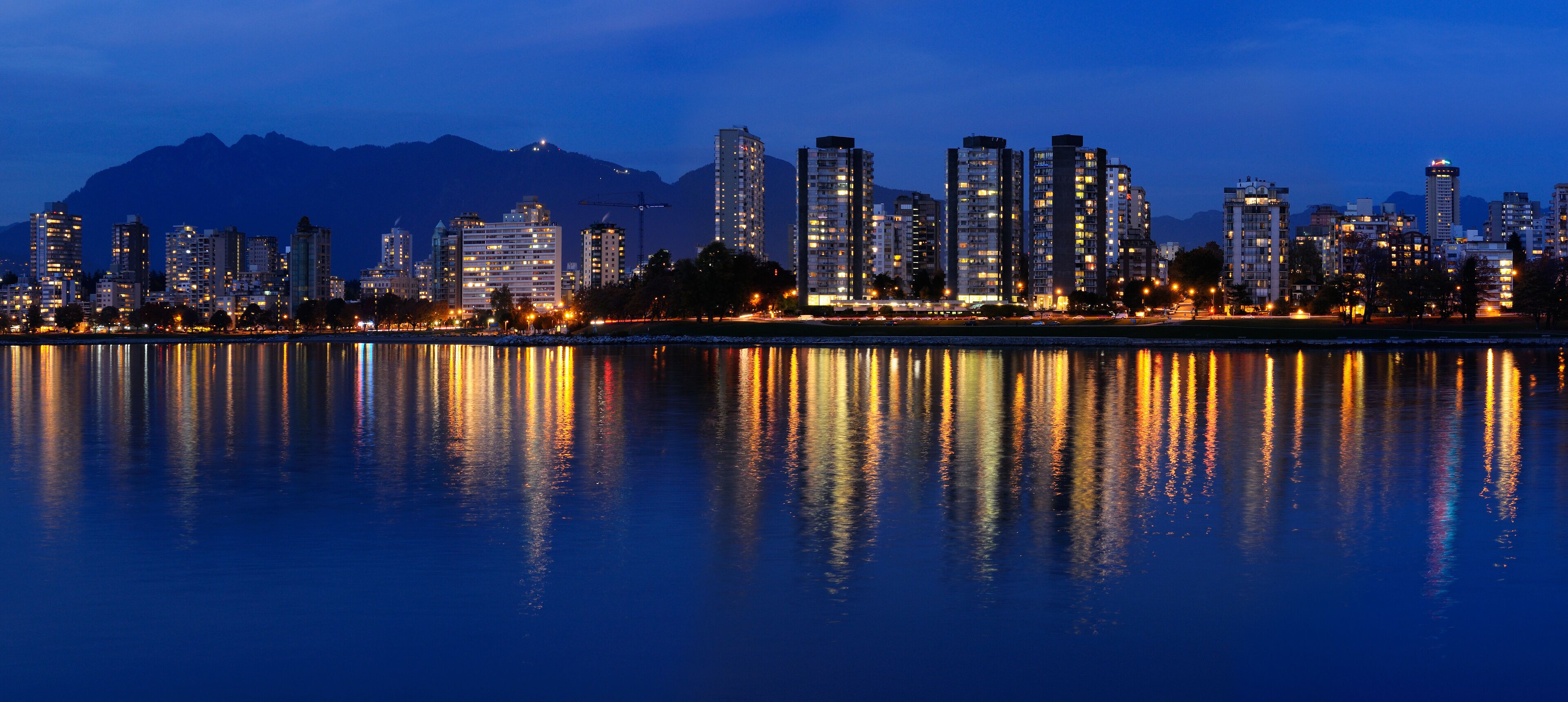 Panorama of West End Vancouver skyline at twilight reflected in English Bay with Grouse Mountain