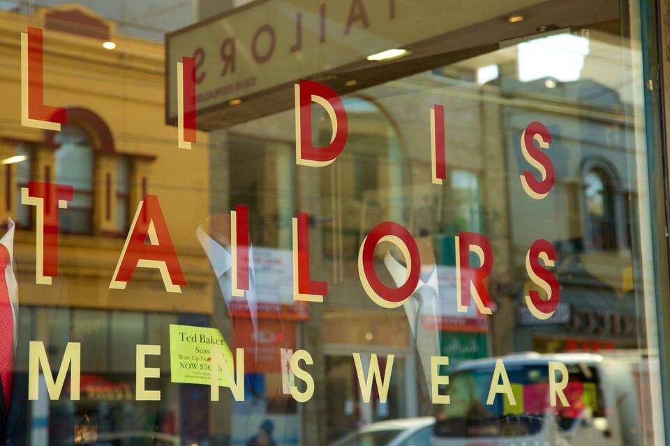 Una vetrina con il cartello "LIDIS TAILORS MEN'SWEAR" e un'etichetta dei prezzi per abiti.