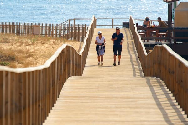 Une promenade en bois qui mène à une plage où l’on peut voir des gens se promener.