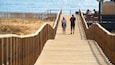 A wooden boardwalk leading to a beach with people walking.