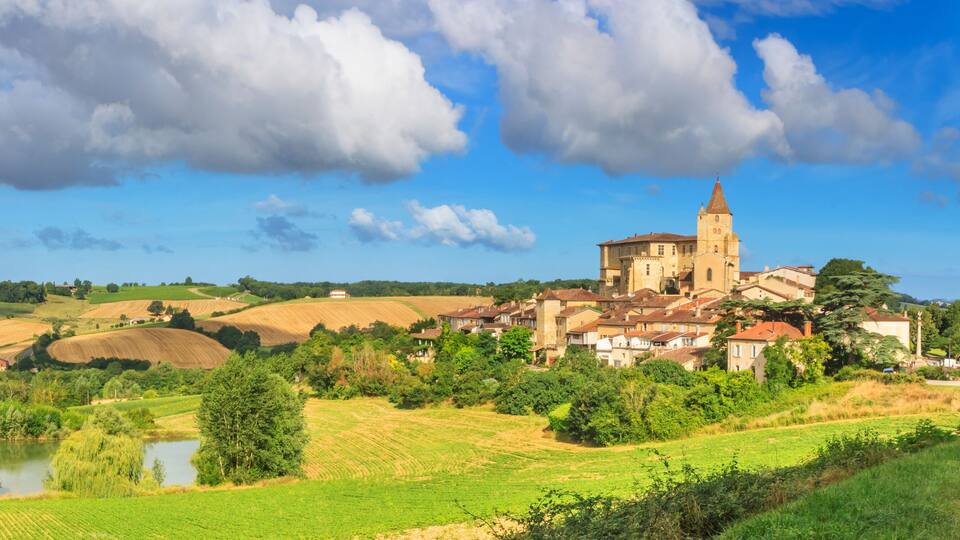 A village with a prominent church, rolling green fields, and a small body of water.