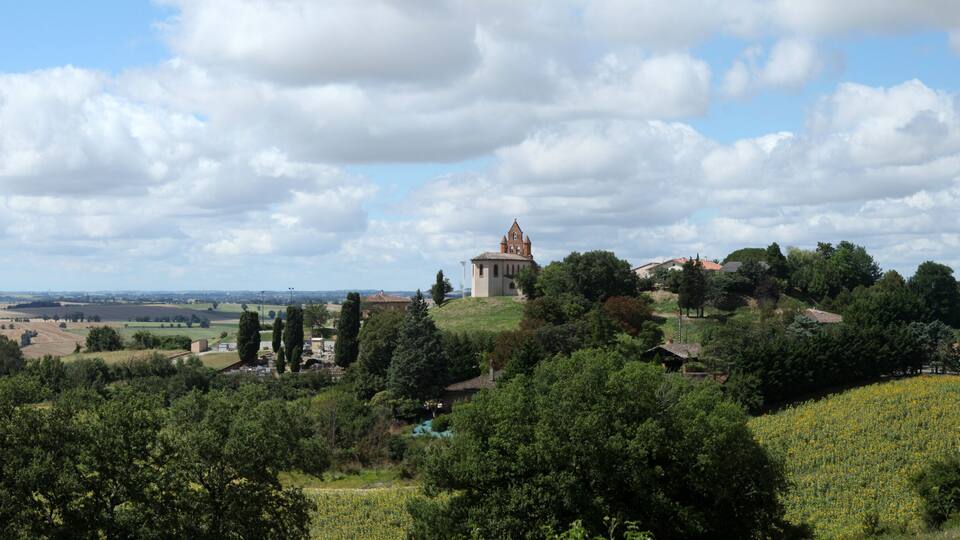 A rural landscape with a church on a hill, surrounded by fields and trees.