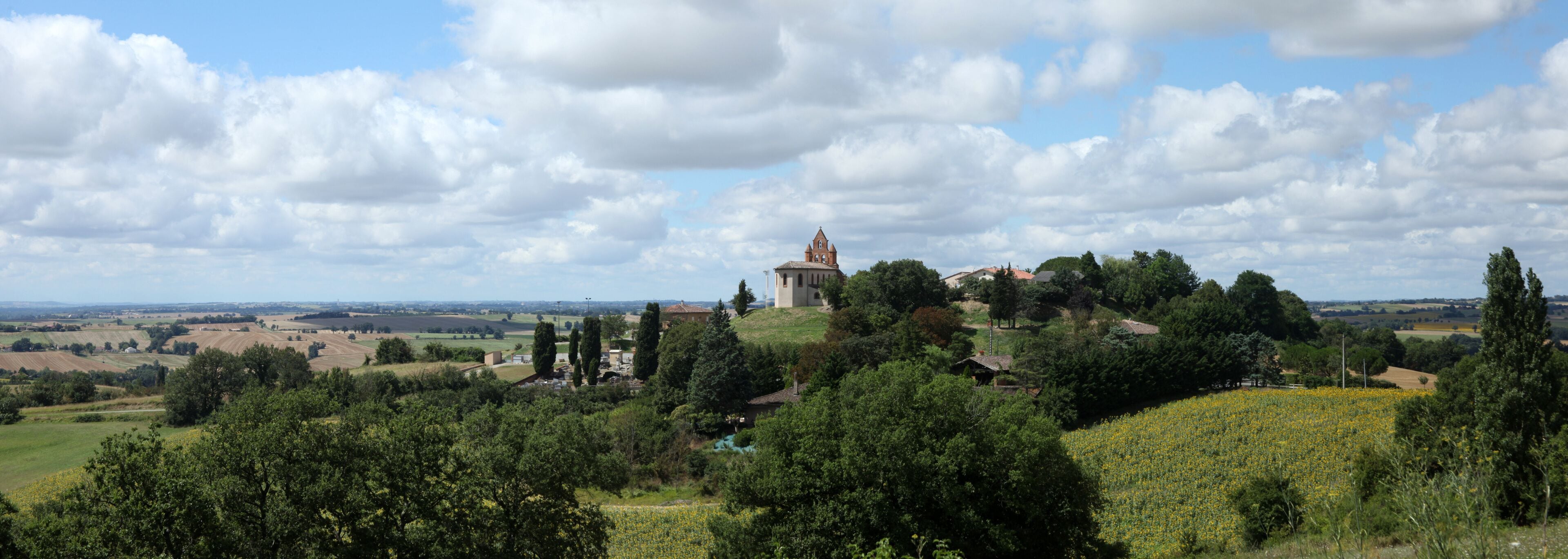 A rural landscape with a church on a hill, surrounded by fields and trees.