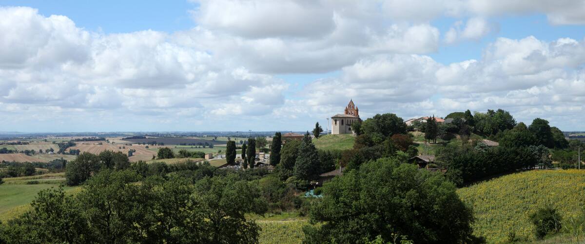 A rural landscape with a church on a hill, surrounded by fields and trees.