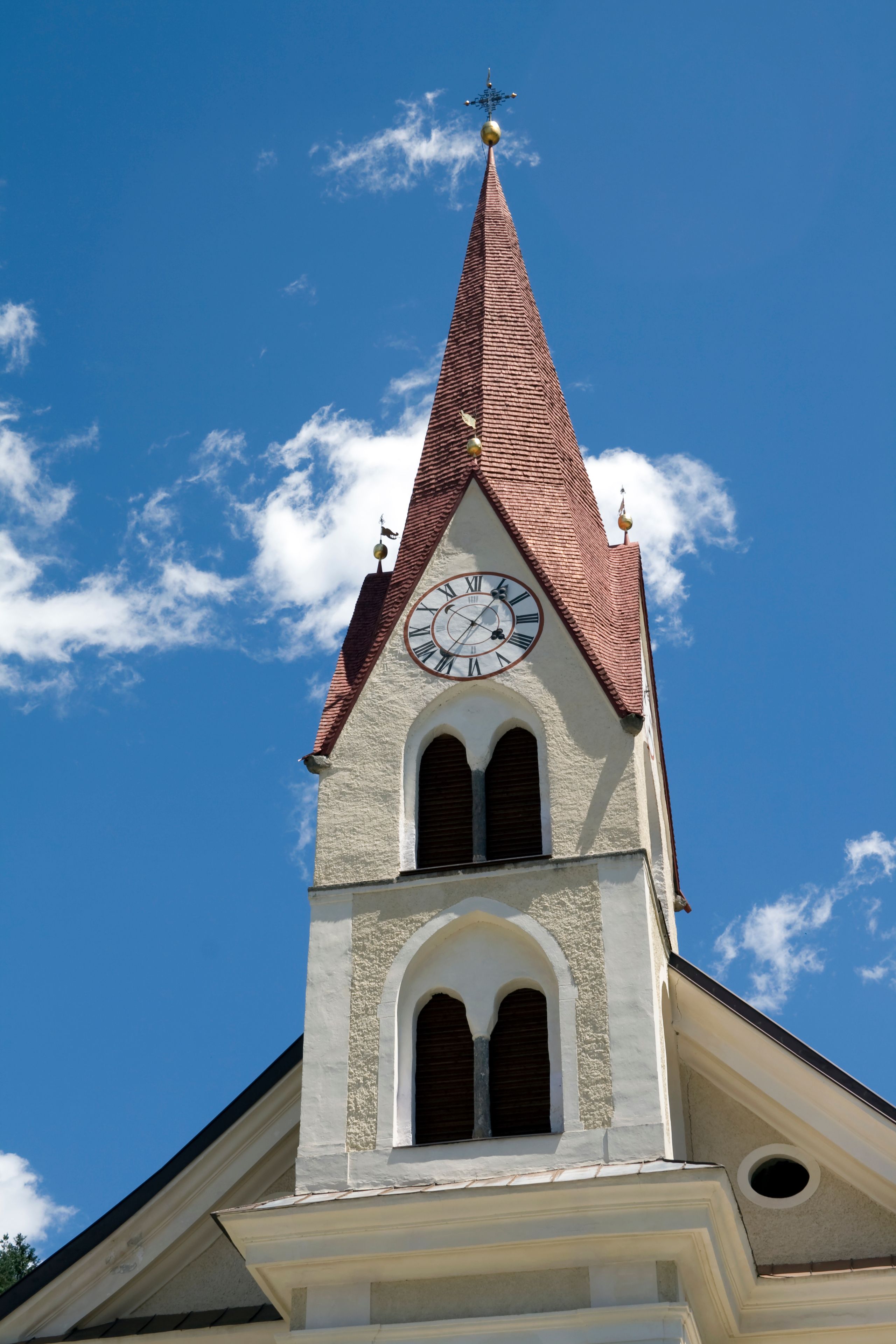 A church tower with a clock, pointed roof, and weather vane.