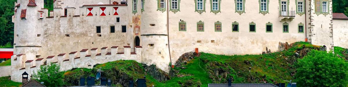 A castle with red-tiled roofs and green window frames, surrounded by lush green forest.