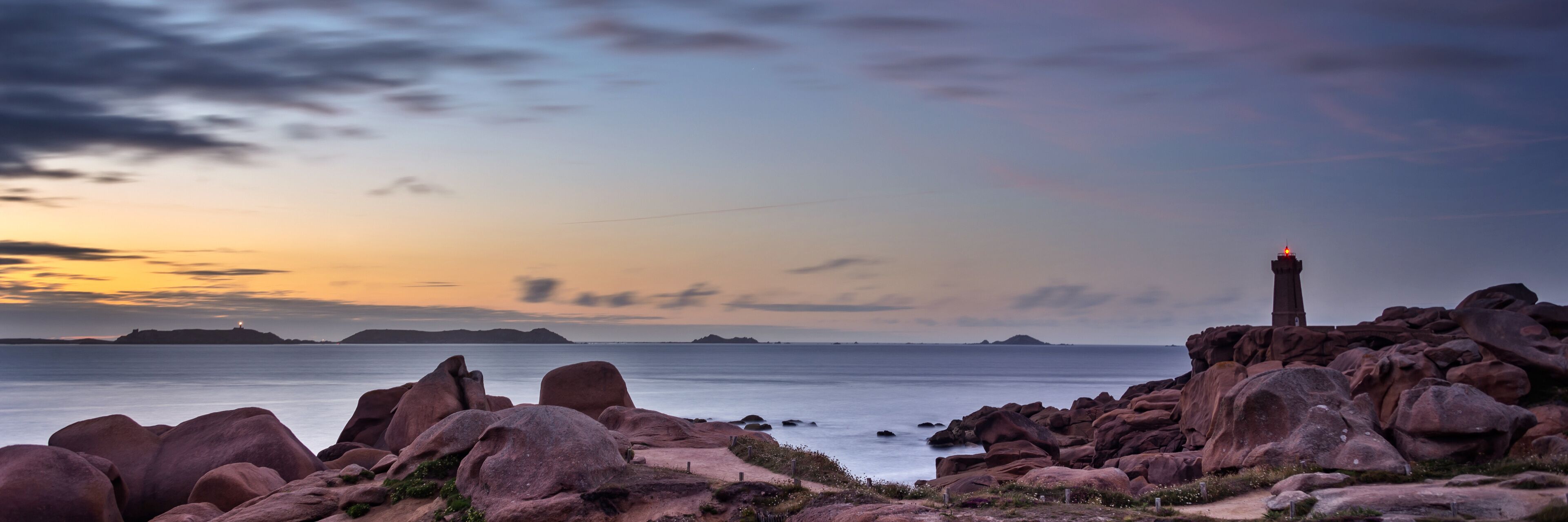 A rocky coastline at sunset with a lighthouse on a cliff.