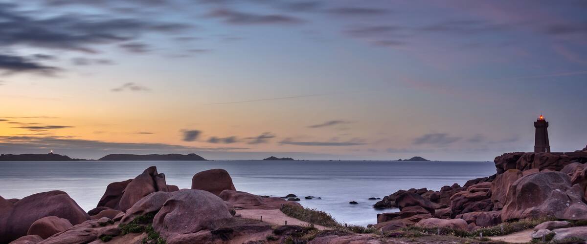 A rocky coastline at sunset with a lighthouse on a cliff.