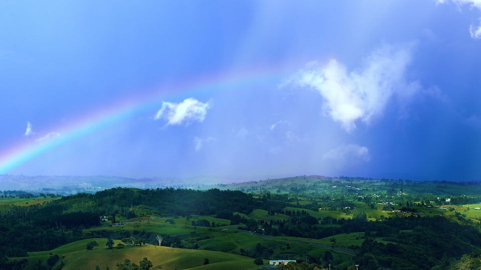 A lush green landscape with rolling hills and a rainbow arching across the sky.