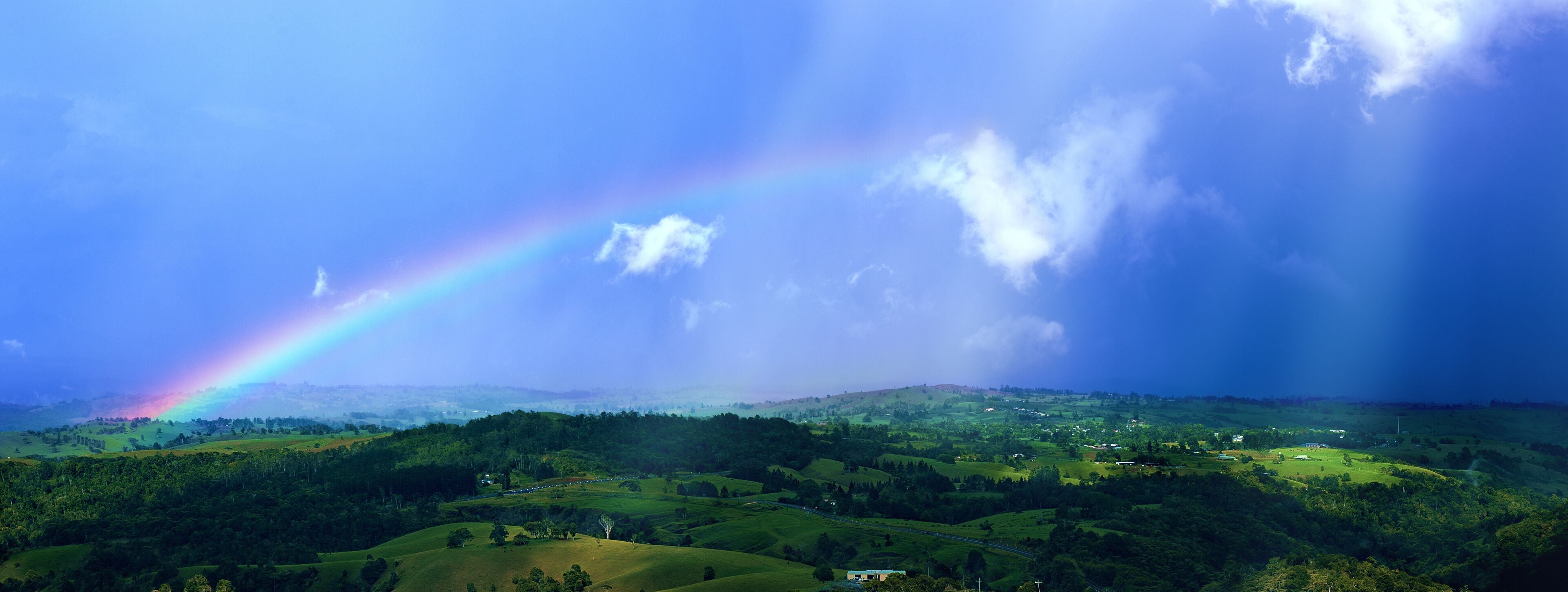 A lush green landscape with rolling hills and a rainbow arching across the sky.