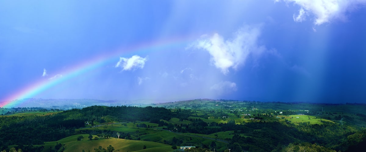 A lush green landscape with rolling hills and a rainbow arching across the sky.