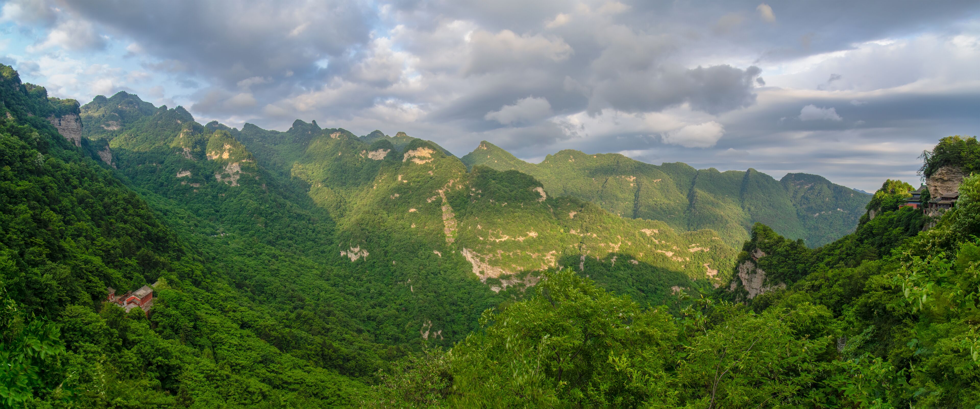A mountainous landscape with dense green forests and rocky cliffs.