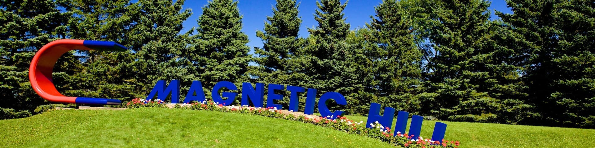 Une zone herbeuse avec un grand panneau bleu sur lequel est écrit en lettres capitales le mot « MAGNÉTIQUE » et une structure rouge et bleue qui ressemble à la lettre « C ».