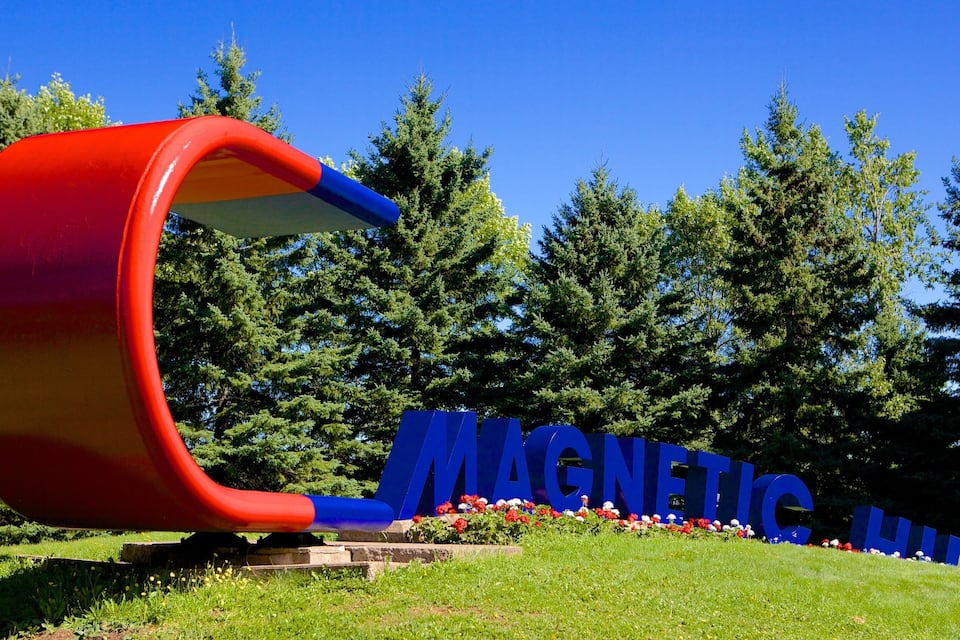 Eine große, rot-blaue Skulptur, die einem Magneten ähnelt, mit den Wörtern „MAGNETIC“ und „MUSIC“ in blauer Schrift, vor dem Hintergrund von Bäumen und blauem Himmel.